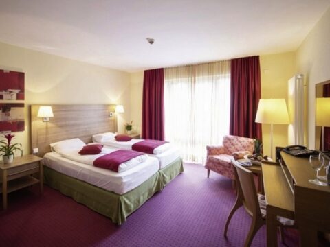 Stilvoll eingerichtetes Zimmer im Nashira Kurpark Hotel für Silvester mit Doppelbett und dekorativem Sessel.