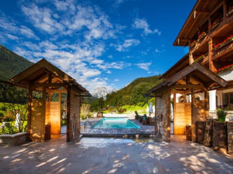 Außenansicht eines Luxushotels mit einem Pool, Holzarchitektur und einer beeindruckenden Alpenkulisse im Hintergrund, ideal für Silvester